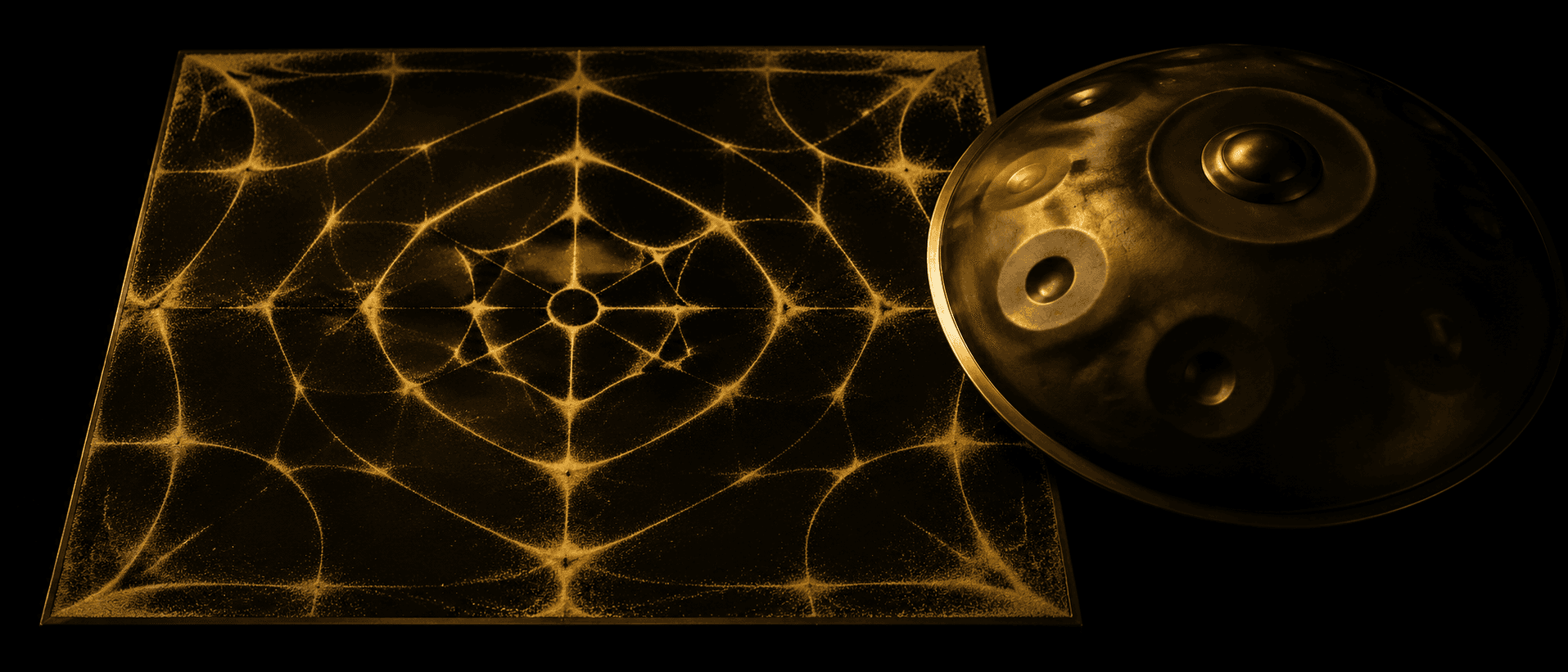 A square steel plate on deep obsidian, fine pale sand pulled into a luminous aurum mandala of nodal lines by a standing wave, a handpan resting against one edge, gold light on black.